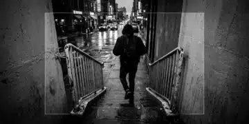 A person in motion, walking up a weathered concrete staircase in a bustling, rain-slicked city street at dusk, reflecting neon green lights, symbolizing business agility and strategic adaptation in dynamic markets.