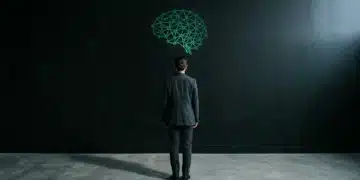 A person viewed from behind, standing before a geometrically patterned matte black wall, with an emerald green neural network light projection, symbolizing the neuroscience of decision-making in modern living.